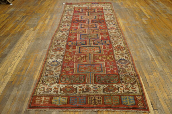 Red and blue geometric runner rug displayed on worn, wide plank hardwood flooring.