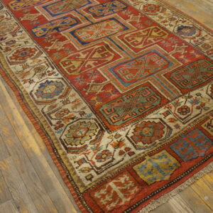 A geometric rug featuring rust red, blue, and gold motifs sits on rustic wood plank flooring.
