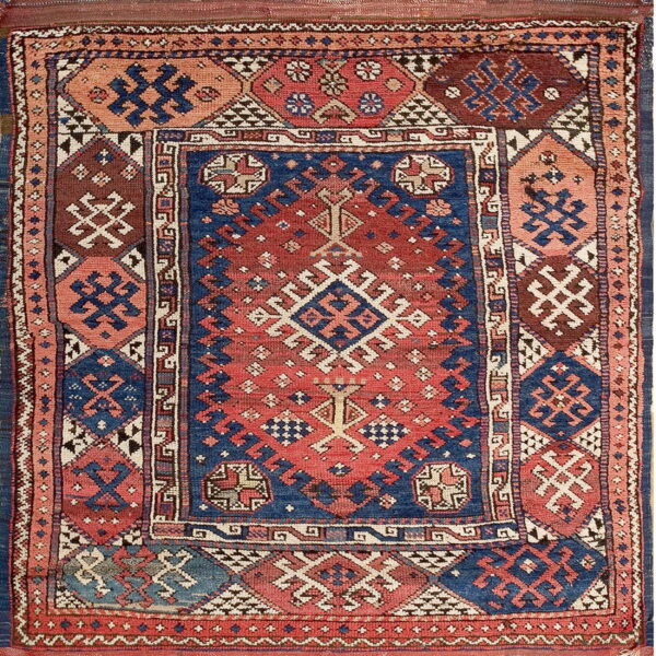 A densely patterned rug featuring geometric designs in red, blue, maroon, and coral colors.