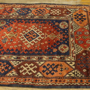 Red and navy geometric tribal rug with complex diamond patterns visible on wide plank wood flooring.
