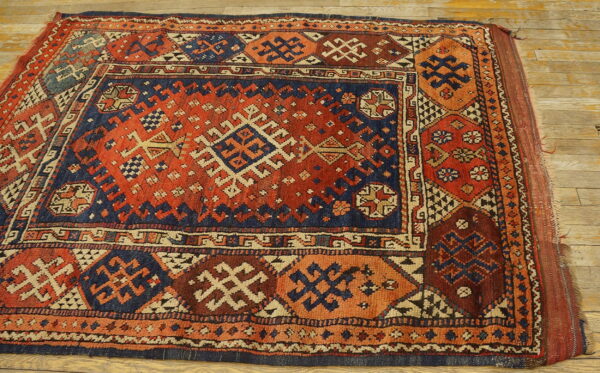 Red and navy geometric tribal rug with complex diamond patterns visible on wide plank wood flooring.
