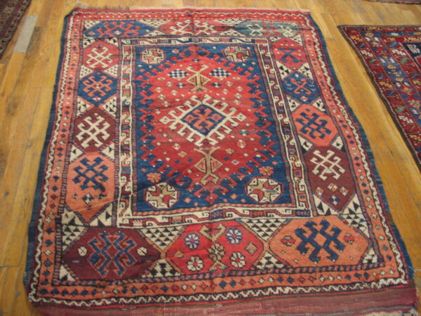A low-pile rug displays intricate red, blue, and cream geometric patterns on light brown hardwood flooring.