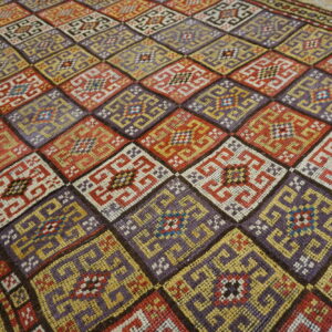 Flatweave rug displaying interlocking geometric designs within alternating red, purple, and yellow diamonds.