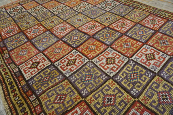 Flatweave rug displaying interlocking geometric designs within alternating red, purple, and yellow diamonds.