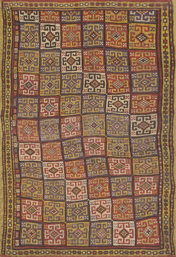 Geometric flatweave rug in a checkerboard pattern of red, purple, gold, and cream stylized squares.