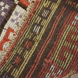 Geometric purple, yellow, and red motifs meet dark brown flatweave stripes on a rustic wooden floor.