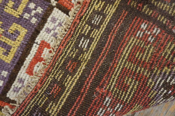 Geometric purple, yellow, and red motifs meet dark brown flatweave stripes on a rustic wooden floor.