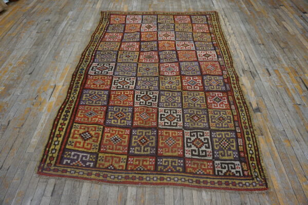 Geometric checkerboard rug in red, purple, gold, and brown colors lying on gray distressed wood flooring.