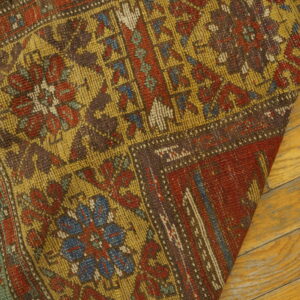 Low-pile rug with faded red, yellow, and blue geometric designs rests on light wood planks.