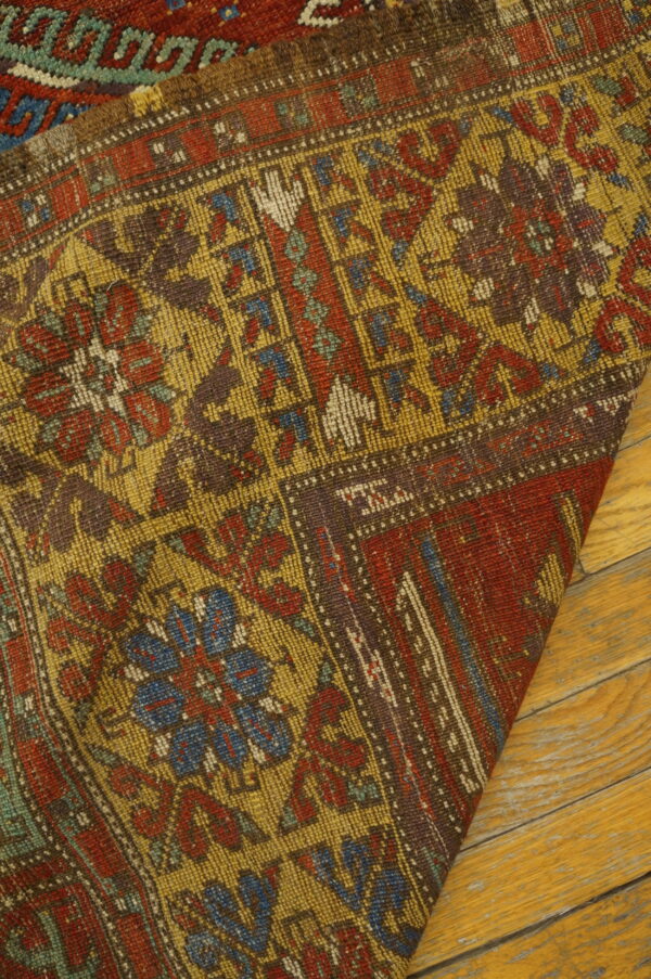 Low-pile rug with faded red, yellow, and blue geometric designs rests on light wood planks.