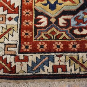 Corner of a multicolored geometric rug, showing red, blue, and cream patterns over distressed wood floor.