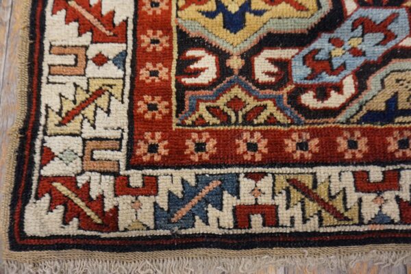 Corner of a multicolored geometric rug, showing red, blue, and cream patterns over distressed wood floor.