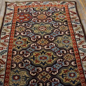 Low-pile rug with complex red, blue, gold, and black geometric motifs on rustic wood planks.
