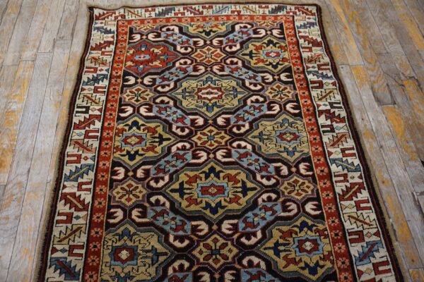 Low-pile rug with complex red, blue, gold, and black geometric motifs on rustic wood planks.