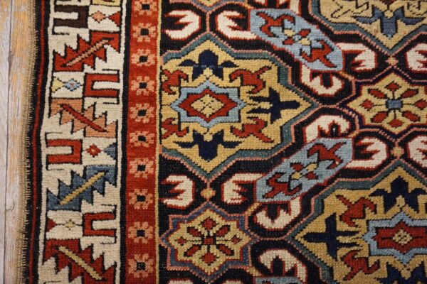 Close-up of a geometric short-pile rug featuring red, navy, gold, and cream on distressed wood flooring.