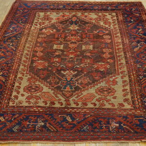 Red, navy, and tan tribal rug with a geometric medallion centered on light wood plank flooring.