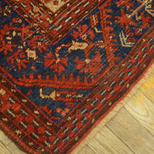 Geometric low-pile rug corner in red, navy, and tan on distressed wood planks.