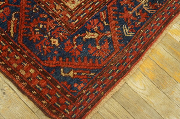 Geometric low-pile rug corner in red, navy, and tan on distressed wood planks.