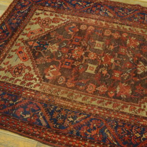 Traditional rug featuring red, brown, tan, and dark blue geometric patterns on light wood planks.