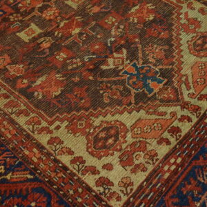Diagonal close-up of a rug featuring geometric patterns in red, brown, tan, and deep blue.