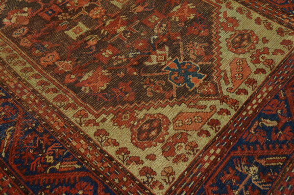 Diagonal close-up of a rug featuring geometric patterns in red, brown, tan, and deep blue.