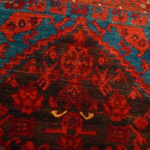 Detailed view of a textured rug featuring red and dark brown geometric patterns on a teal background.