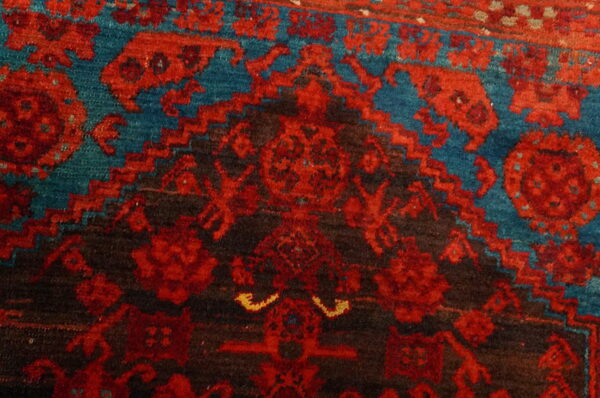 Detailed view of a textured rug featuring red and dark brown geometric patterns on a teal background.