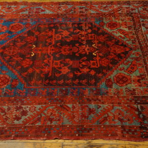 Ornate red, dark brown, and faded blue geometric rug featuring a central medallion on wood plank flooring.