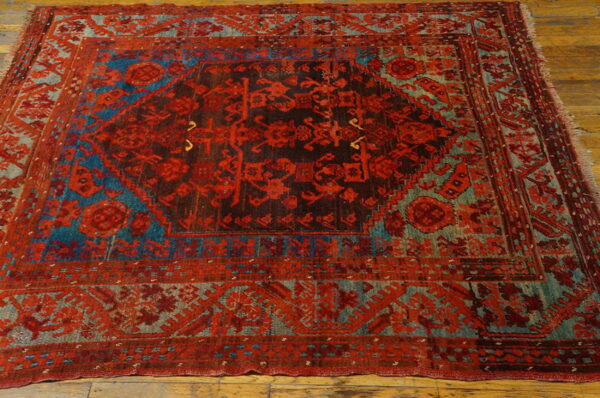 Ornate red, dark brown, and faded blue geometric rug featuring a central medallion on wood plank flooring.