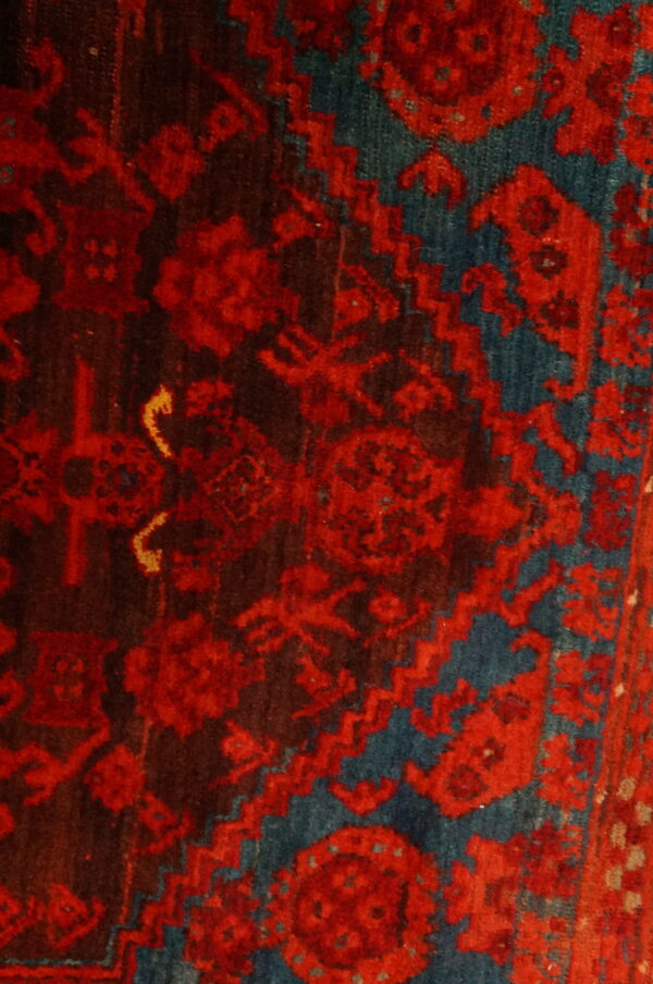 Close-up of a high-pile rug showing dense traditional motifs in bright red, dark brown, and teal blue.