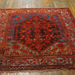 A patterned square rug in red, brown, and bright blue tones rests on distressed wooden floor planks.