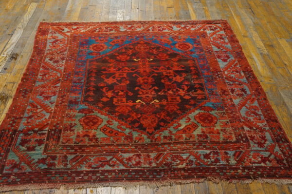A patterned square rug in red, brown, and bright blue tones rests on distressed wooden floor planks.