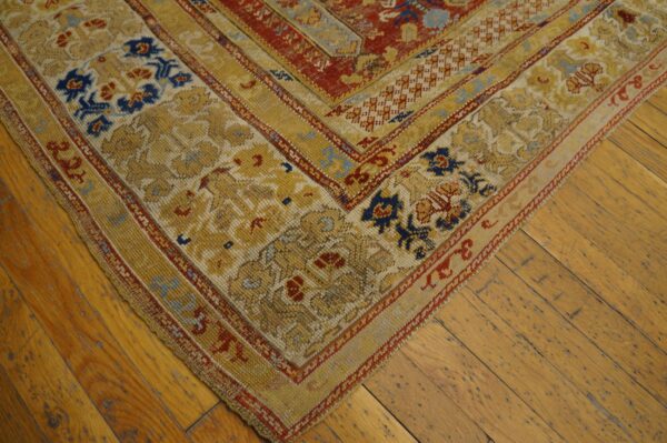 A corner of a traditional gold, red, and blue low-pile rug lies on distressed wood plank flooring.