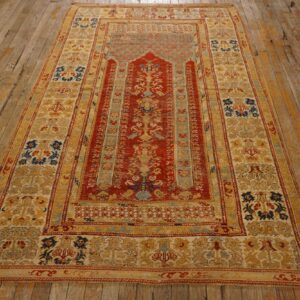 Red and gold patterned rug laid on worn, wide plank wooden floorboards.