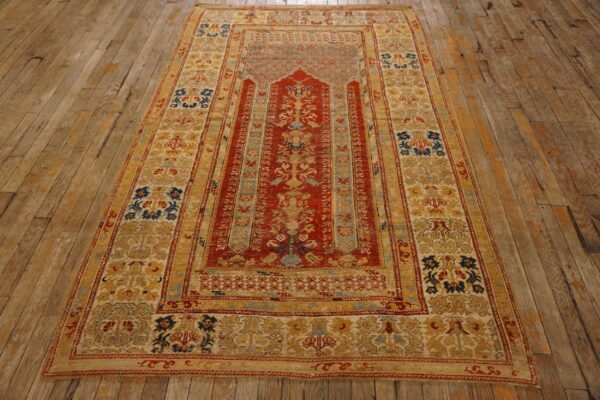 Red and gold patterned rug laid on worn, wide plank wooden floorboards.