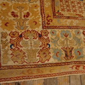 Low-pile rug corner featuring mustard, cream, red, and blue floral motifs on rustic wood planks.