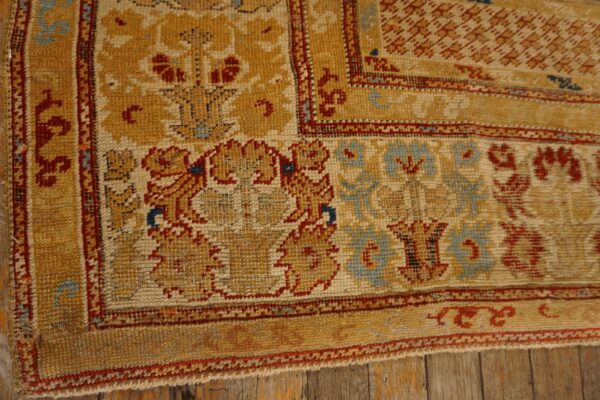 Low-pile rug corner featuring mustard, cream, red, and blue floral motifs on rustic wood planks.