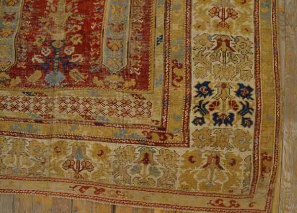 Distressed rug corner featuring dense red and gold patterns with blue details on wood flooring.