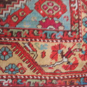Woven rug detail with red and blue floral medallions set against a tan geometric field.