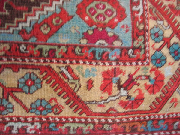Woven rug detail with red and blue floral medallions set against a tan geometric field.