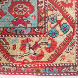 Detailed corner of a rug with intricate red, blue, and tan traditional patterns over wood flooring.