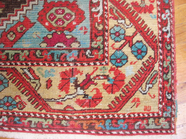 Detailed corner of a rug with intricate red, blue, and tan traditional patterns over wood flooring.