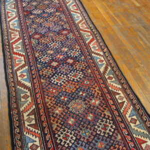 A geometric blue, red, and cream runner rug is placed diagonally on plank wood flooring.