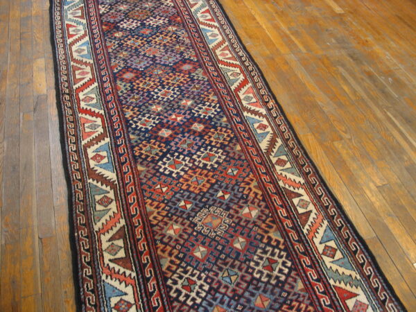 A geometric blue, red, and cream runner rug is placed diagonally on plank wood flooring.