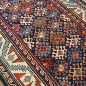 Geometric rug featuring deep blue, rust, light blue, and cream tribal motifs on hardwood flooring.