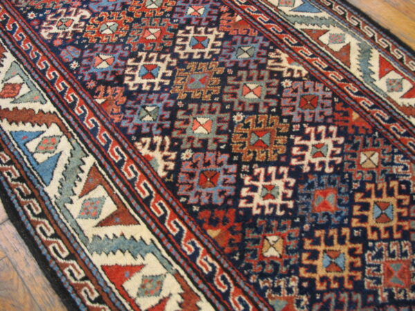 Geometric rug featuring deep blue, rust, light blue, and cream tribal motifs on hardwood flooring.