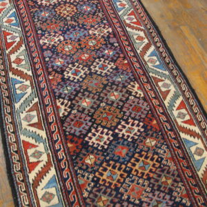 Geometric navy runner rug with red, cream, and blue designs lies on glossy wood flooring.