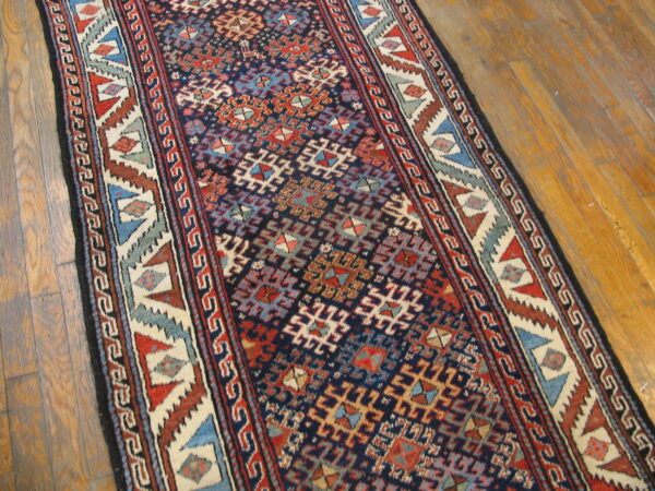 Geometric navy runner rug with red, cream, and blue designs lies on glossy wood flooring.