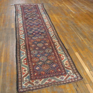 Navy and red geometric runner with stepped motifs and low pile resting on distressed wood flooring.