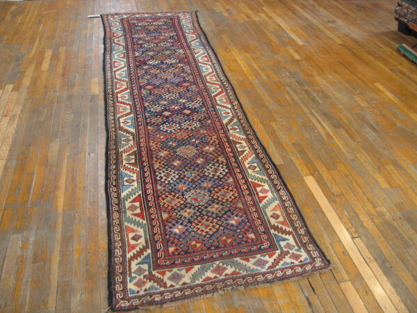 Navy and red geometric runner with stepped motifs and low pile resting on distressed wood flooring.